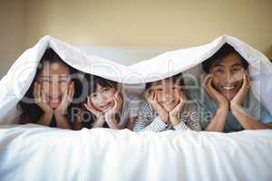 Family relaxing together under a blanket in bedroom