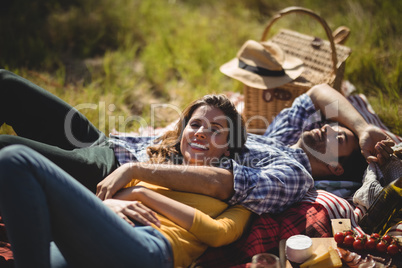Smiling young woman with boyfriend relaxing on picnic blanket at olive farm