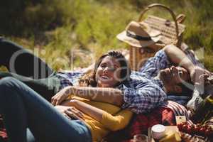 Smiling young woman with boyfriend relaxing on picnic blanket at olive farm