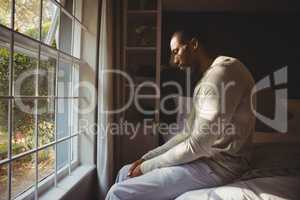 Side view of sad man sitting on bed by window