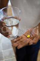 Mid section of senior man holding drinking water and medicines