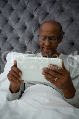 Senior man using digital tablet while resting on bed