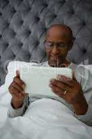 Senior man using digital tablet while resting on bed