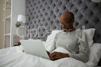 Senior man using laptop while sitting on bed