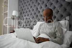 Senior man using laptop while sitting on bed