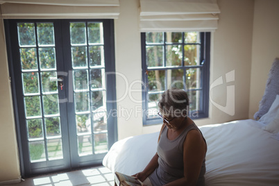 Senior woman reading book while sitting on bed in the bed room