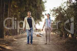 Portrait of couple carrying basket while walking on dirt road at olive farm
