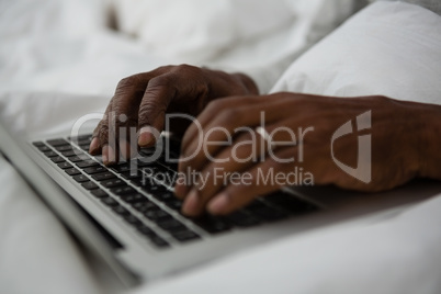 Cropped hands of man using laptop on bed