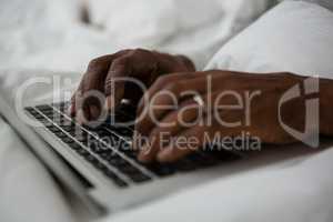 Cropped hands of man using laptop on bed
