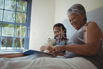 Grandmother and granddaughter watching photo album together in bed room