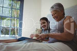 Grandmother and granddaughter watching photo album together in bed room