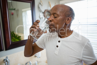 Senior man taking medicine while standing in bathroom