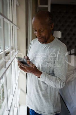 Smiling senior man using mobile phone by window at home