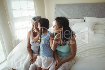 Daughter kissing grandmother on cheeks in bed room