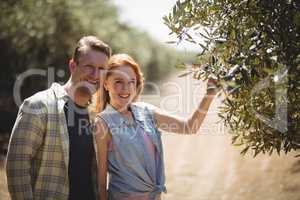 Smiling young couple standing by olive tree at farm