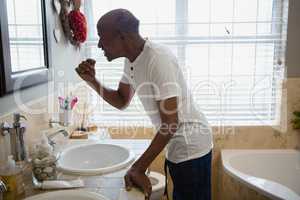 Senior man brushing teeth by sink in bathroom