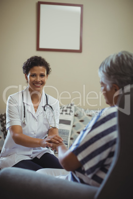 Female doctor comforting senior woman in living room