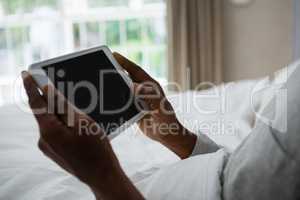 Mid section of senior man holding digital tablet on bed