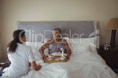 Female doctor serving breakfast to senior woman on bed