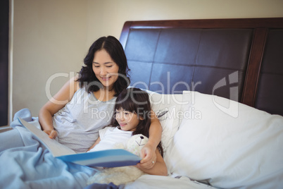 Mother and daughter reading book on bed in bed room