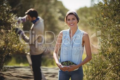 Smiling woman carrying olives with man in background at farm