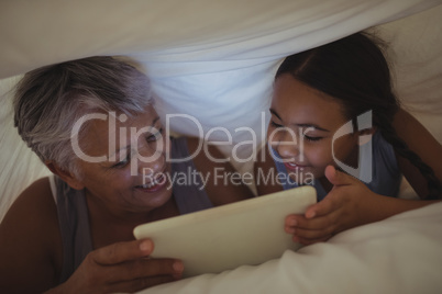 Grandmother and granddaughter using digital tablet in bed room