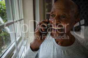 Happy senior man talking on mobile phone by window
