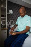 Senior man holding medicines while sitting in bedroom at home