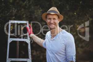 Smiling young man with ladder standing at olive farm