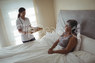 Female doctor serving breakfast to senior woman on bed