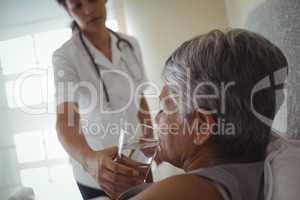 Female doctor giving sick senior woman a glass of water on bed