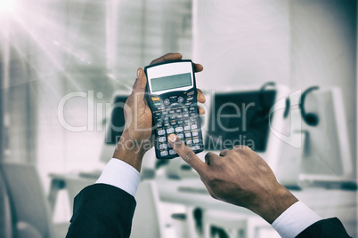 Composite image of cropped hands of businessman using calculator