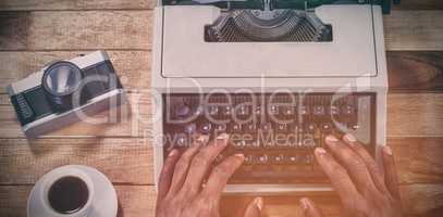 Cropped hands of businessman using typewriter by vintage camera and coffee