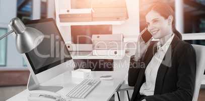Composite image of smiling businesswoman talking on mobile phone at desk with computer