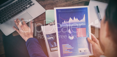 Businesswoman analyzing graphs with laptop on table