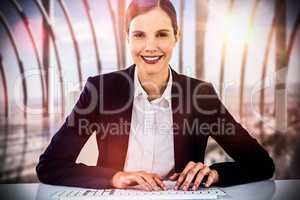 Composite image of portrait of smiling businesswoman typing on keyboard at desk