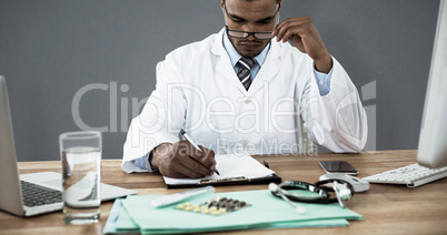 Composite image of doctor writing on clipboard at desk