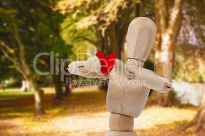 Composite image of wooden 3d figurine standing and holding a red heart in front