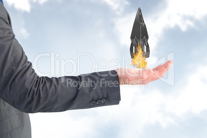 Businessman holding a rocket taking off from his hand against sky background