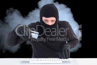 Hacker wearing hood is holding a credit card in the smoke against black background