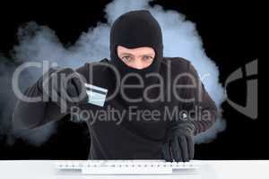 Hacker wearing hood is holding a credit card in the smoke against black background