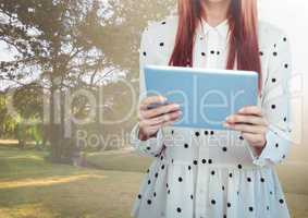 Woman mid section with polka dot top and tablet against park with flares