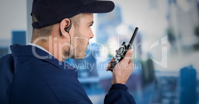 Security guard with cap and walkie talkie against blurry window showing city