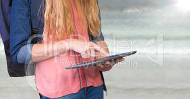 Woman mid section with backpack and tablet against blurry beach and flare
