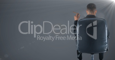 Back of seated business man smoking cigar against grey background with flare
