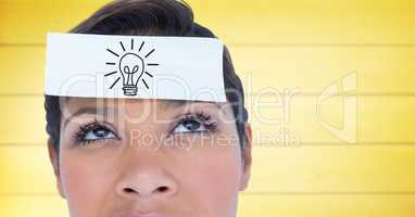 Close up of woman with card on head lightbulb doodle against blurry yellow wood panel