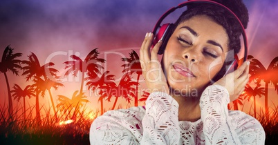 Happy casual woman listenning music with headphones in front of plam trees background