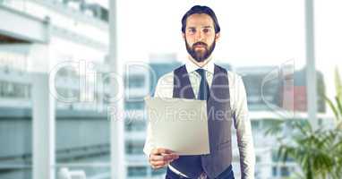 Creative businessman holding paper while standing in office against defocused buildings
