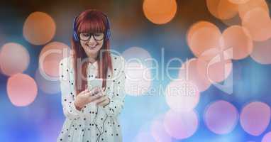 Smiling beautiful woman listening music through headphones while standing against defocused lights