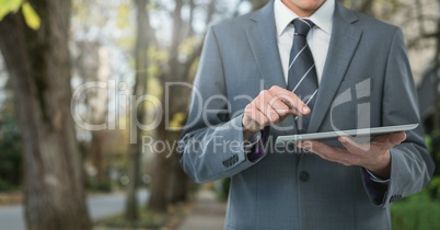 Businessman holding tablet on path with trees